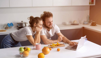 年轻的夫妇烹饪健康的食物厨房首页女孩靠男人。微笑看<strong>浪漫</strong>的<strong>电影</strong>美丽的年轻的夫妇会说话的视频调用移动PC