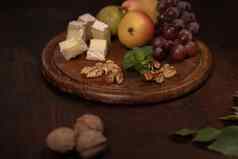 布里干酪奶酪水果葡萄核桃黑暗木板木董事会酒零食集选择奶酪葡萄梨核桃木表格一边角视图