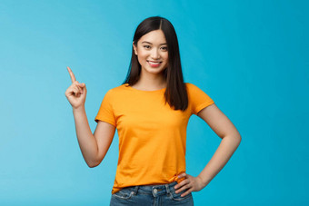 快乐自信亚洲女孩自信的指出上左角落里显示微笑确定自信的介绍在线商店促销站蓝色的背景黄色的t恤