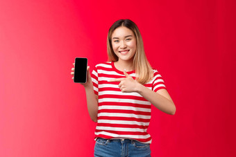 满意快乐的可爱的亚洲金发碧眼的女孩微笑广泛的显示智能<strong>手机</strong>显示指出电话屏幕很高兴介绍太棒了<strong>应用</strong>程序推荐<strong>应用</strong>程序红色的背景