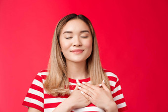 爱温暖的女孩心温柔的浪漫的亚洲女人关闭眼睛感情满意乐观的新闻手胸部微笑放松令人愉快的还记得不错的记忆感觉和平幸福红色的背景