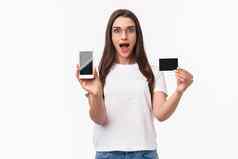 肖像兴奋快乐年轻的女人介绍应用程序最喜欢的在线商店买衣服显示移动电话信贷卡微笑逗乐白色背景