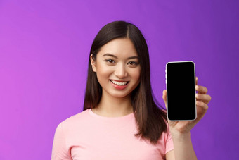 特写镜头有吸引力的愉快的女商店助理现在电话应用程序持有智能手机显示电话屏幕介绍应用程序显示站紫色的背景很高兴