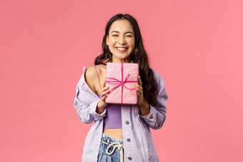 肖像快乐的快乐亚洲女孩收到礼物微笑兴奋持有包装现在隐藏幸福庆祝生日邀请生日聚会，派对粉红色的背景