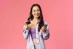 肖像年轻的时尚的女孩微笑很高兴相机移动电话持有信贷卡支付在线购买商店互联网订单食物交付站粉红色的背景