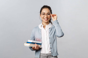 教育老<strong>师大</strong>学学校概念年轻的女学生亚洲女孩研究考试修复眼镜眼睛微笑携带书图书馆站灰色背景