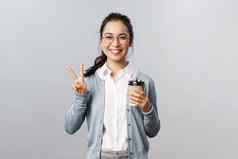 办公室生活方式业务人概念乐观友善的亚洲女孩显示和平标志微笑卡哇伊享受早....新鲜的杯咖啡当地的咖啡馆站灰色背景