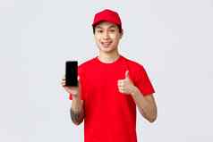 交付应用程序在线购物航运概念英俊的亚洲快递红色的t恤帽显示翘拇指批准移动电话屏幕应用程序提供快质量服务