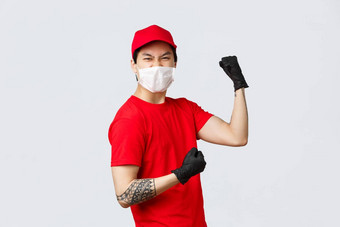 热情的亚洲交付的家伙红色的统一的帽t恤穿保护手套医疗面具提高信心拳头泵庆祝成功准备好了转移包裹客户