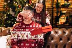 微笑年轻的女人覆盖眼睛微笑好奇的丈夫给包装盒子圣诞节礼物装饰节日树一年冬天假期家庭庆祝活动假期奇迹
