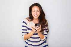 微笑年轻的亚洲女人持有手机灰色的墙