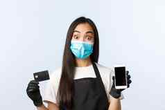 科维德流感大流行咖啡商店小业务防止病毒概念兴奋惊讶亚洲咖啡馆工人医疗面具手套显示信贷卡移动电话