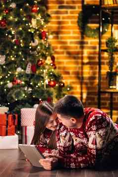 高加索人夫妇男人。女人休息首页发光的一年树打字平板电脑圣诞节礼物在线假期销售买在线出售现代科技过度使用概念