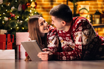 高加索人家庭夫妇选择圣诞节现在在线平板电脑说谎舒适的首页丈夫妻子圣诞节礼物平板电脑电脑设备一年精神假期庆祝活动