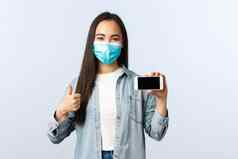 社会距离生活方式科维德流感大流行技术概念满意朝鲜文女孩医疗面具竖起大拇指推荐智能手机应用程序移动电话商店