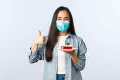 社会距离生活方式科维德流感大流行庆祝假期冠状病毒概念快乐微笑亚洲生日女孩医疗面具显示bday蛋糕翘拇指很高兴
