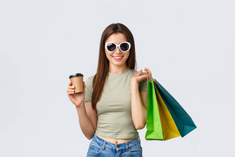 购物购物中心生活方式旅游时尚概念时尚的无忧无虑的女人太阳镜喝咖啡购买衣服持有外卖杯商店袋