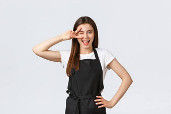 杂货店商店员工小业务咖啡商店概念乐观友好的可爱的咖啡师黑色的围裙显示和平标志眼睛微笑邀请游客咖啡馆餐厅