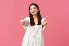 美人情绪夏天休闲假期概念友好的快乐的亚洲女孩微笑显示竖起大拇指推荐太棒了酒店水疗中心度假胜地粉红色的背景