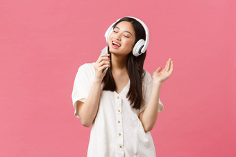 美人情绪技术概念无忧无虑的快乐亚洲女孩移动<strong>电话卡</strong>拉ok应用程序唱歌智能手机麦克风听音乐耳机粉红色的背景