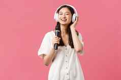 美人情绪技术概念无忧无虑的快乐亚洲女孩移动电话卡拉ok应用程序唱歌麦克风听音乐耳机粉红色的背景