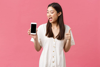 美人情绪技术概念兴奋快乐亚洲女孩博主演示太棒了应用程序feautre显示移动电话屏幕竖起大拇指喜乐粉红色的背景