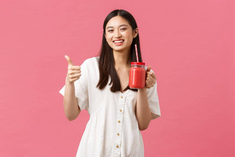 健康的食物情绪夏天生活方式概念乐观的快乐满意女咖啡馆游客享受美味的奶昔显示竖起大拇指推荐喝粉红色的背景