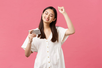 美人情绪技术概念女孩享受看最喜欢的韩国流行音乐音乐视频智能手机跳舞击败移动电话高喊粉红色的背景