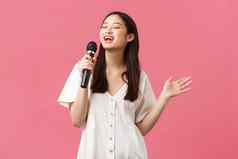 休闲人情绪生活方式概念无忧无虑的漂亮的亚洲女孩时尚的衣服唱歌首歌麦克风享受卡拉ok晚上有趣的粉红色的背景