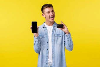 技术生活方式广告概念英俊的微笑男人。介绍功能应用程序显示信贷卡移动电话屏幕很高兴脸黄色的背景