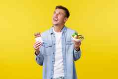 健康的生活方式人食物概念快乐梦幻微笑的家伙上左角落里持有碗沙拉糖果酒吧站黄色的背景