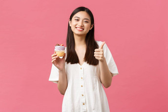 食物咖啡馆餐厅夏天生活方式概念快乐亚洲女人满意太棒了味道甜点竖起大拇指推荐蛋糕面包店商店站粉红色的背景