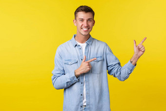 英俊的微笑快乐男人。白色牙齿指出手指邀请客户检查广告演示产品特殊的折扣提供了站黄色的背景