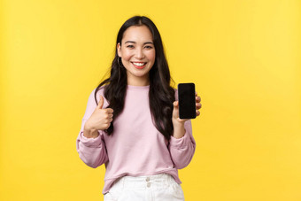 人情绪生活方式休闲美概念微笑亚洲女人显示智能手机显示推荐应用程序移动游戏显示竖起大拇指批准黄色的背景