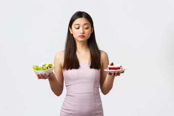 健康的生活方式休闲食物概念美丽的亚洲女孩<strong>抵制</strong>诱惑咬甜蜜的美味的蛋糕完整的卡路里住饮食吃沙拉白色背景