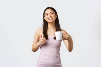 生活方式人情绪魅力概念华丽的亚洲女人喝咖啡显示竖起大拇指微笑很高兴享受喝站白色背景