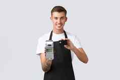 零售业务咖啡馆餐厅员工概念英俊的微笑服务员显示非接触式支付持有回来终端信贷卡站黑色的围裙白色背景