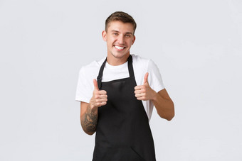 员工杂货店商店咖啡商店概念英俊的友好的的家伙工人咖啡馆商店职员穿黑色的围裙显示竖起大拇指微笑客人保证质量