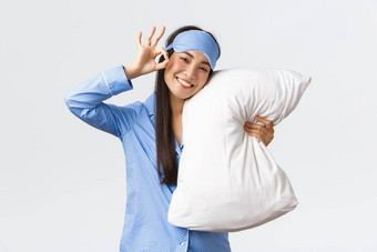 满意快乐微笑可爱的亚洲女孩蓝色的睡衣睡觉<strong>眼膜</strong>拥抱枕头面具显示手势推荐产品药物治疗睡眠白色背景