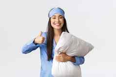 快乐的很高兴可爱的亚洲女孩蓝色的睡衣睡觉面具持有软舒适的枕头显示竖起大拇指满意好晚上睡眠采取药片失眠