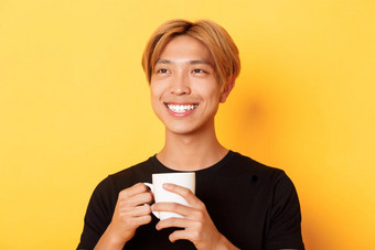 特写镜头快乐微笑英俊的金发碧眼的亚洲的家伙梦幻怀旧喝咖啡站黄色的背景