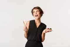 快乐的有吸引力的女人参加庆祝活动聚会，派对持有玻璃香槟一块蛋糕站白色背景