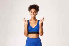 概念体育运动锻炼微笑非裔美国人女运动员快乐充满希望的使手指交叉站白色背景蓝色的运动服装