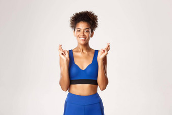 概念体育运动锻炼微笑非裔美国人女运动员快乐充满希望的使手指交叉站白色背景蓝色的运动服装