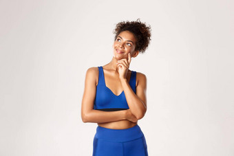 工作室拍摄深思熟虑的微笑非裔美国人健身女人穿蓝色的体育运动装<strong>上</strong>左角落里很高兴微笑思考白色背景
