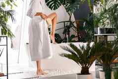 裁剪拍摄年轻的女人白色浴袍持有腿一边浴缸干刷牙皮肤