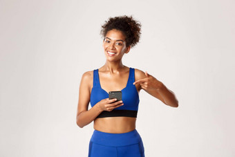 体育运动技术概念有吸引力的非裔美国人健身女人运动服装指出手指移动电话推荐锻炼应用程序白色背景