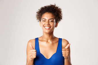 快乐的非裔美国人女运动员锻炼服装显示竖起大拇指眨眼推荐体育运动白色背景