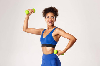 概念体育运动锻炼适合健康的非裔美国人健身女人锻炼哑铃健身房转头微笑站白色背景