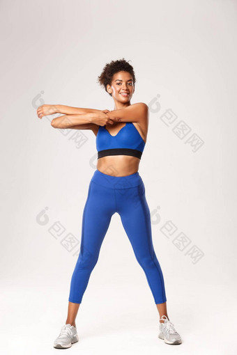 完整的长度微笑运动非裔美国人女运动员穿蓝色的体育运动装伸展运动健身活动锻炼白色背景